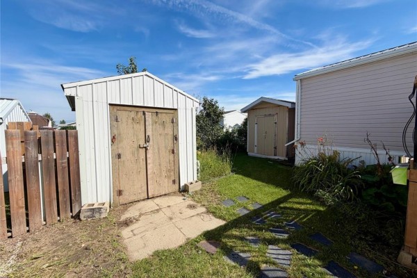 White storage shed with double wooden doors and a wooden fence in the backyard of the property. - 323 Glen Avenue, Brandon