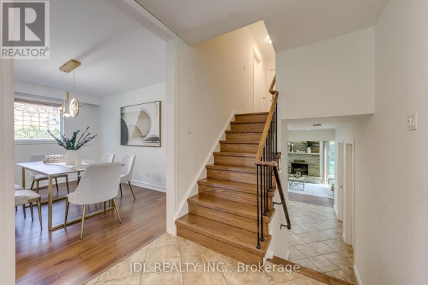 Hallway with hardwood stairs, tiled floor, and doorways to dining and living areas. - 323 Warminster Drive S, Oakville
