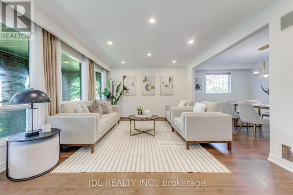 Living room with light-colored sofas, coffee table, rug, and large windows. - 323 Warminster Drive S, Oakville