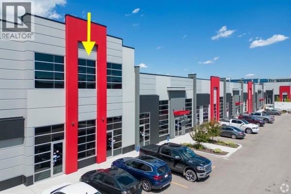 Exterior view of modern commercial building with grey, black, and red facade, and parking lot. - 3235, 6520 36 Street Ne, Calgary