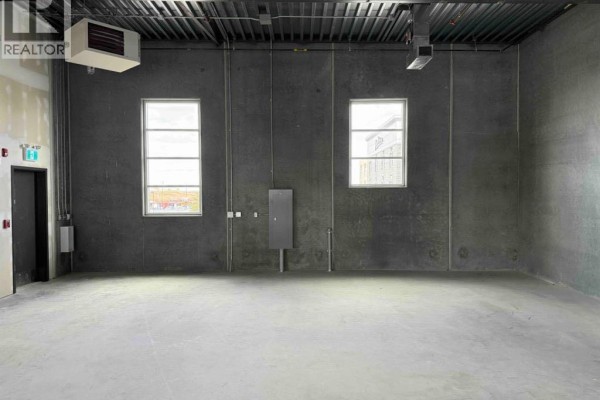 Interior commercial space with concrete floor, dark grey walls, two windows, and an industrial heater. - 3235, 6520 36 Street Ne, Calgary