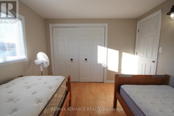 Bedroom with two twin beds, light wood floors, double white closet doors, a closed white door, and a fan. - 323d Grahamvale Road, Chisholm