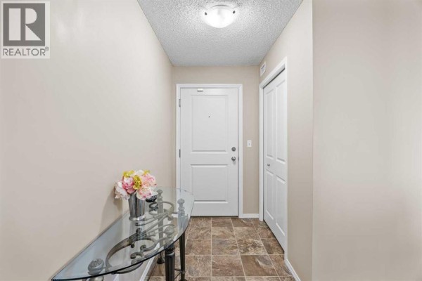 Apartment entryway with beige walls, tiled floor, glass console table, and white double doors. - 324, 195 Kincora Glen Road Nw, Calgary