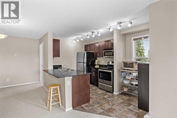Kitchen with dark wood cabinets, granite countertops, stainless steel appliances, and a breakfast bar. - 324, 195 Kincora Glen Road Nw, Calgary