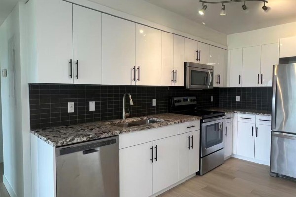 A bedroom with a bed, white dresser, and a large window with a view of buildings. - 324 235 Bridgeland Drive, Winnipeg