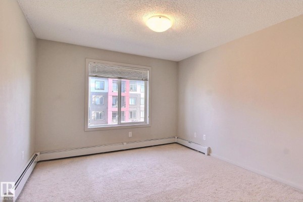 Open concept living area with island, dark wood floors, and sliding balcony doors. - #324 344 Windermere Rd Nw, Edmonton