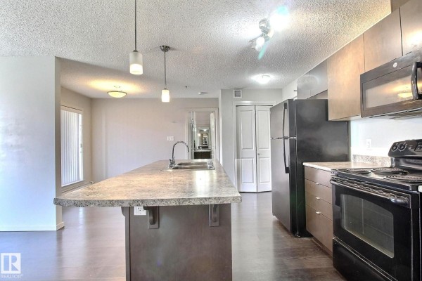 Kitchen with dark cabinets, stainless steel appliances, island with sink, and doorway to living area. - #324 344 Windermere Rd Nw, Edmonton