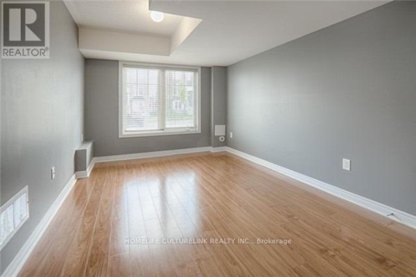 Empty room with light wood floors, gray walls, and a large window with blinds on the right. - 324 Delray Drive, Markham