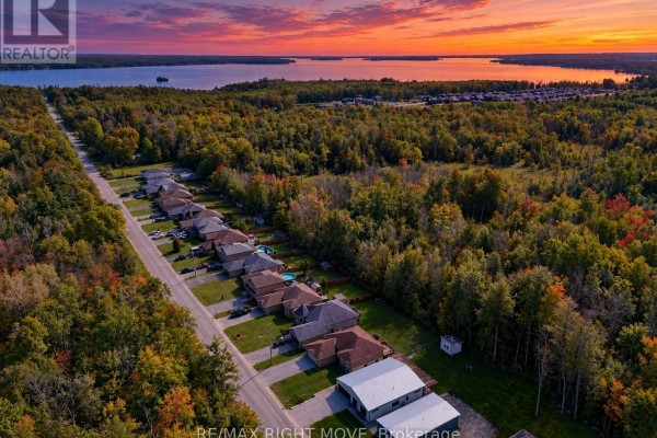 Aerial view of a suburban street lined with houses and trees, with a large lake in the distance. - 3240 Goldstein Road, Severn