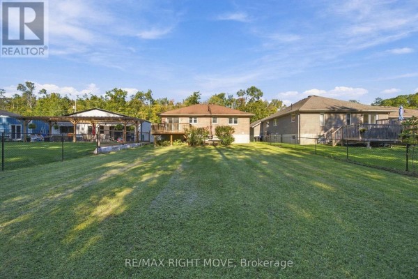Rear view of a backyard with green grass, a wooden deck, and adjacent homes, bordered by a black fence. - 3240 Goldstein Road, Severn