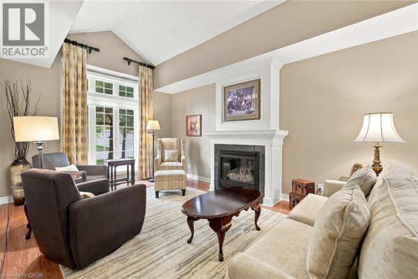 A living room with hardwood floors, a neutral-toned sofa, armchair, and decorative fireplace. - 3241 Montrose Road Unit# 22, Niagara Falls