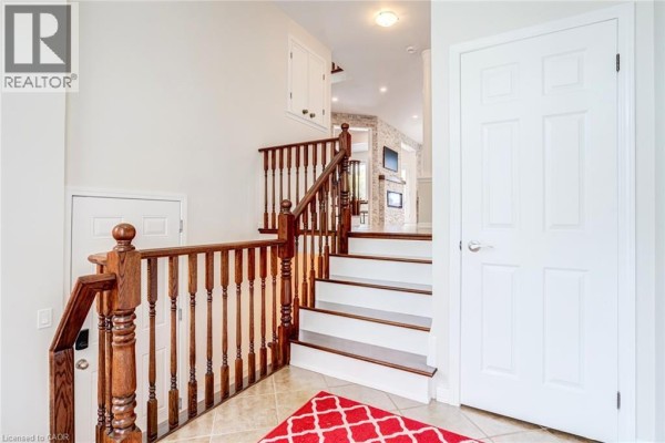Interior foyer with a wooden staircase, beige tiled floor, and white doors. - 3244 Steeplechase Drive, Burlington