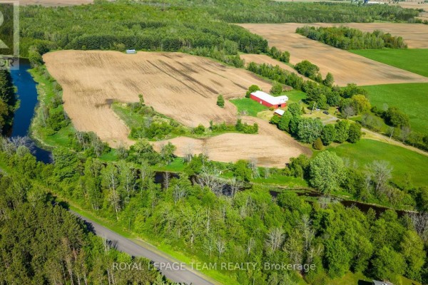 Aerial view of a farm with red barn and fields by a river. - 3245 Wallace Road, North Dundas
