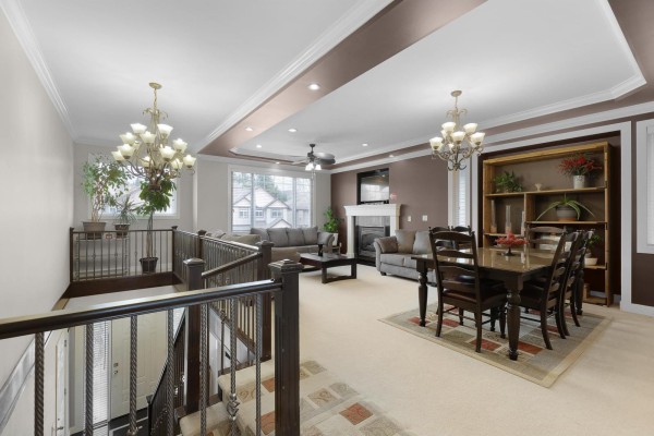 Living room and dining room with beige carpet, brown walls, and two chandeliers. - 32460 Mitchell Avenue, Mission
