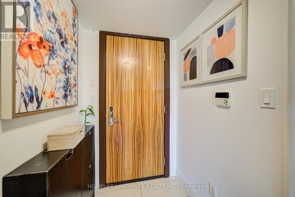 Apartment entrance door with wood grain finish, flanked by abstract art and a dark cabinet. - 325 - 50 Clegg Road, Markham
