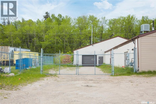 View down a paved street with commercial buildings on the left and right, including a long blue building. - 325 17th Street W, Prince Albert