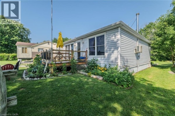 Side exterior of 325 Blue Water Parkway, a light blue cottage with windows, deck, and garden. - 325 Blue Water Parkway, Selkirk