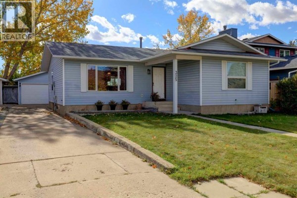 Side view of a light blue bungalow with a paved driveway and green lawn. - 325 Flett Drive Ne, Airdrie