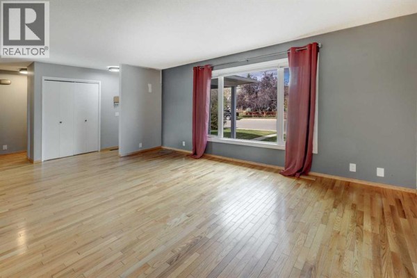 Spacious living room with hardwood floors, grey walls, and large windows with maroon curtains. - 325 Flett Drive Ne, Airdrie