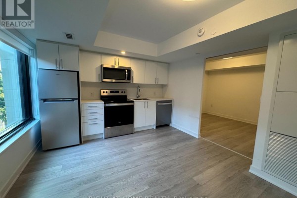 Kitchenette with stainless steel appliances, white cabinets, and light wood floors. - 326 - 3 Strathgowan Avenue, Toronto