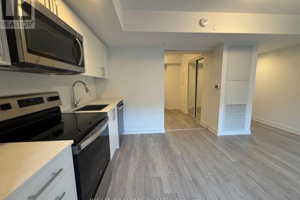 View of apartment kitchenette and hallway with light wood floors and white walls. - 326 - 3 Strathgowan Avenue, Toronto