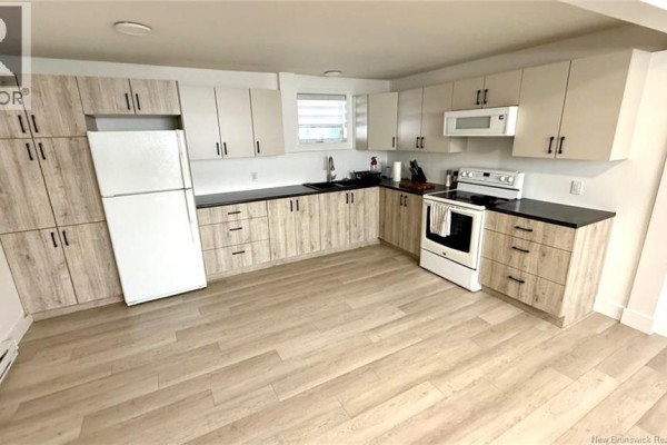 Small bathroom with a white vanity, toilet, tiled shower area with a white curtain, and patterned wall tiles. - 326 1ere Rue, Shippagan