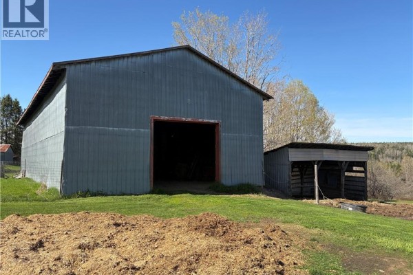 Interior view of a spacious barn with wooden stalls, hay, and farm equipment, looking towards the open entrance. - 326 Dorn Ridge Road, Burtts Corner