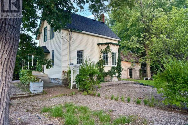 Side exterior view of the house showing clapboard siding, windows, and overgrown greenery. - 326 Third Street E, Cornwall