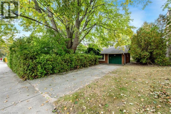 Exterior of a house with a detached garage, concrete driveway, and lush green foliage. - 326 Walkers Line, Burlington