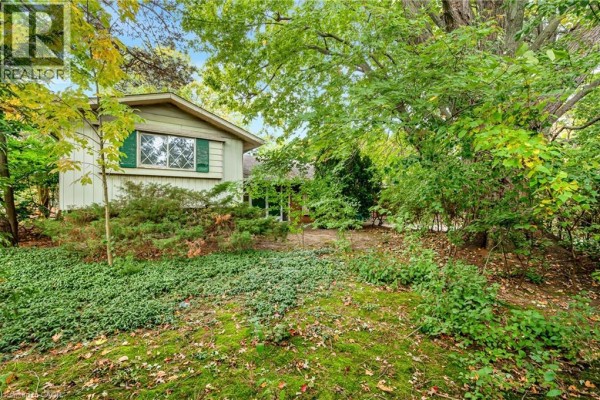 View of the house exterior featuring light green siding, a window with green shutters, and abundant greenery. - 326 Walkers Line, Burlington