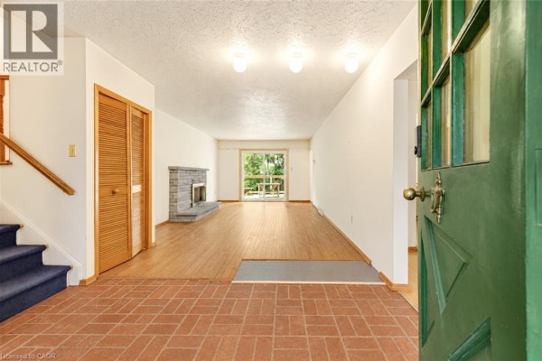 Foyer area with terracotta tile flooring, blue carpeted stairs, a fireplace, and an opening to the living room. - 326 Walkers Line, Burlington