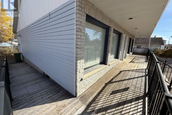 Close-up view of the wooden exterior ramp with black metal railings, next to a paved walkway. - 3261 Petawawa Boulevard, Petawawa