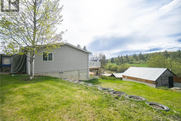 Kitchen with wooden cabinets, white appliances, and a laundry area in the corner. - 327 97a Highway, Spallumcheen