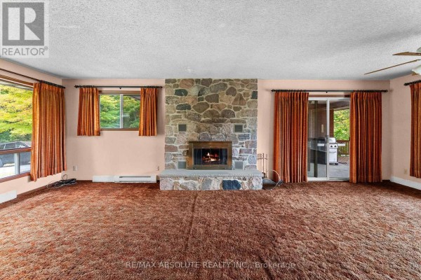 Living room with a large stone fireplace, brown carpet, peach walls, and sliding glass doors to a deck. - 327 Nieman Drive, Mcnab/braeside
