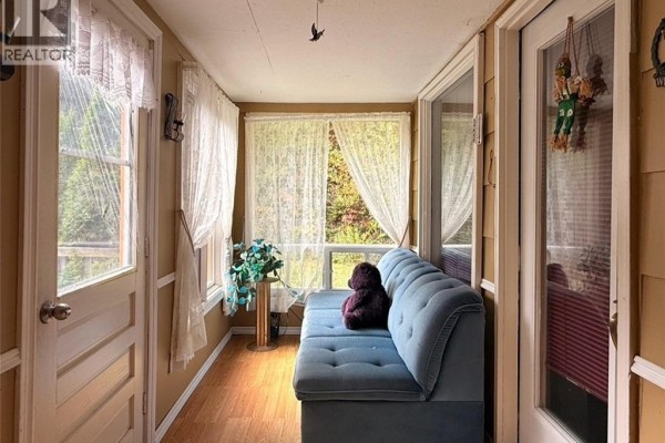 Sunroom with a blue couch, floor-to-ceiling windows, and white lace curtains. - 355 St Maure Road, Balmoral
