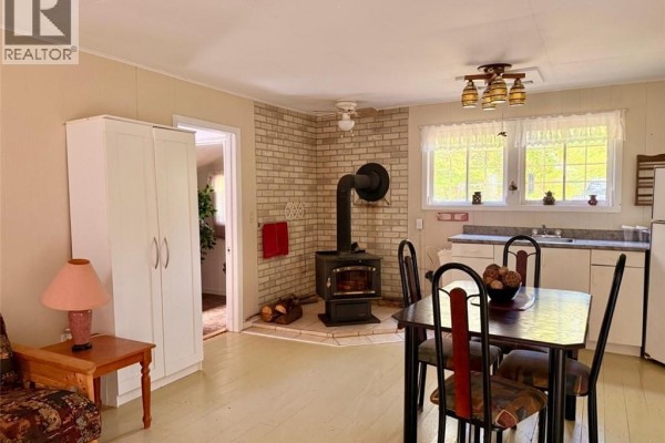 Living and dining area with a wood-burning stove, white cabinets, and a dining table. - 355 St Maure Road, Balmoral