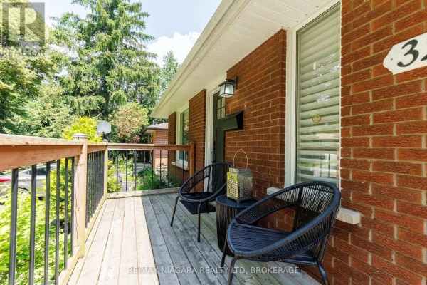 Front view of a brick bungalow with a manicured lawn, driveway, and surrounding trees. - 3273 Addison Avenue, Niagara Falls