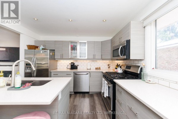 Modern kitchen with grey cabinets, stainless steel appliances, white quartz island, and pink stools. - 3273 Addison Avenue, Niagara Falls