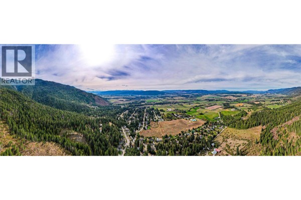 Panoramic aerial view of a valley with mountains, forest, fields, and a residential area. - 3275 Upper Mcleod Road, Spallumcheen