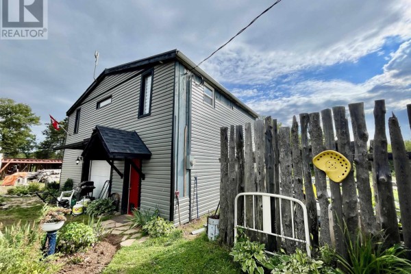 Side view of the house with grey vinyl siding and a wooden fence. - 32756 Route 2, Springhill