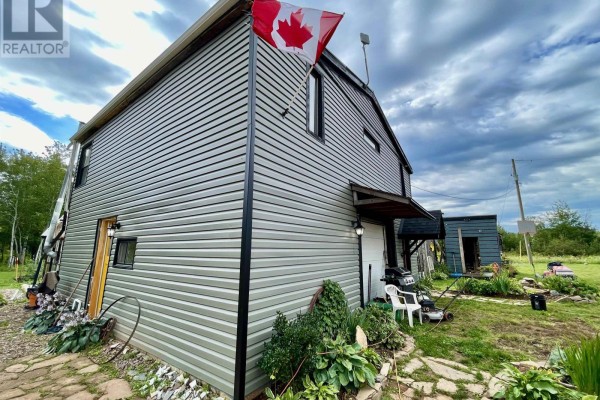 Back side of the house with grey vinyl siding and a Canadian flag. - 32756 Route 2, Springhill