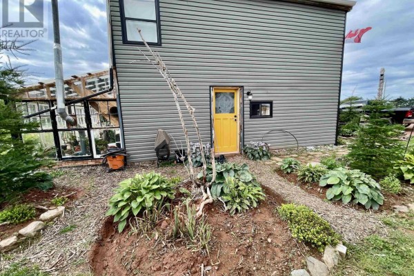 Rear exterior of the house with a yellow door and a greenhouse. - 32756 Route 2, Springhill
