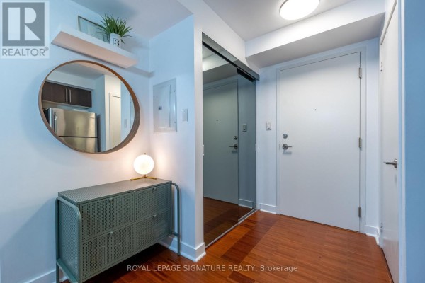 Apartment entryway with white walls, hardwood floors, and a mirrored closet door. - 328 - 1169 Queen Street W, Toronto