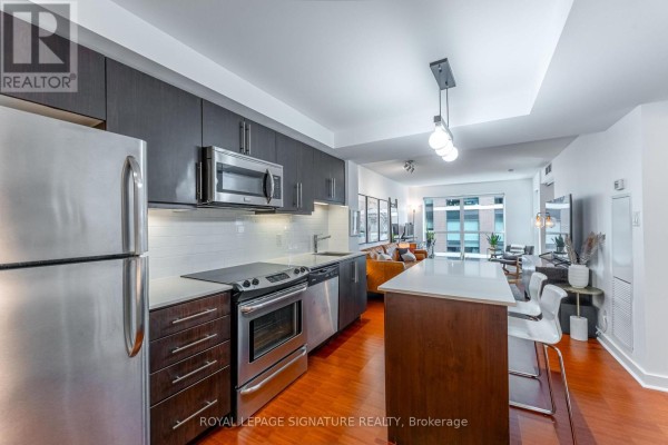 Kitchen with stainless steel appliances, dark wood cabinets, and a white island. - 328 - 1169 Queen Street W, Toronto