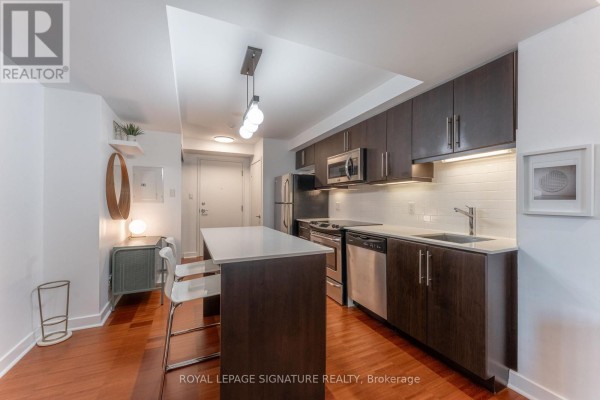 Kitchen area with dark wood cabinets, white countertop, and stainless steel appliances. - 328 - 1169 Queen Street W, Toronto