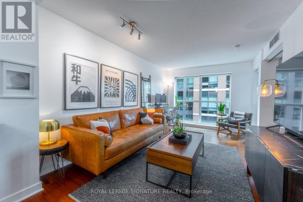 Living room with a brown leather sofa, coffee table, and large window with city view. - 328 - 1169 Queen Street W, Toronto