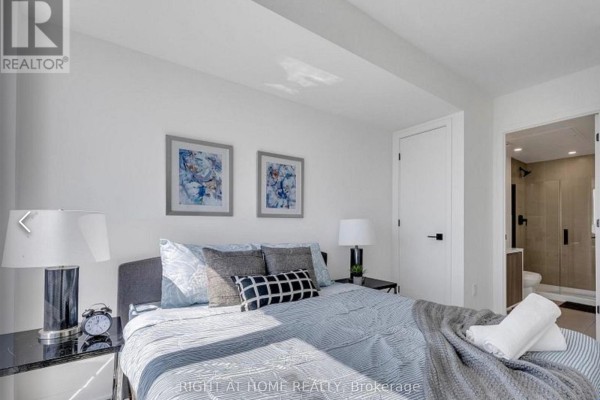 Bedroom with a grey upholstered bed, white walls, and two framed abstract art pieces. - 328 - 36 Zorra Street, Toronto