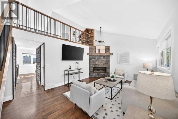 Living room with vaulted ceiling, stone fireplace, mounted television, and loft overlook with bookshelves. - 328 3 Street Ne, Calgary