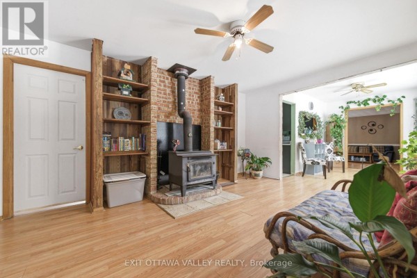 Living room with light wood flooring, a brick fireplace, wood shelving, and a sofa. - 32848 Highway 17 Highway, Laurentian Hills