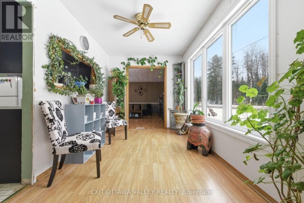 Living room with wood flooring, a stove, a sofa with red pillows, and plants. - 32848 Highway 17 Highway, Laurentian Hills